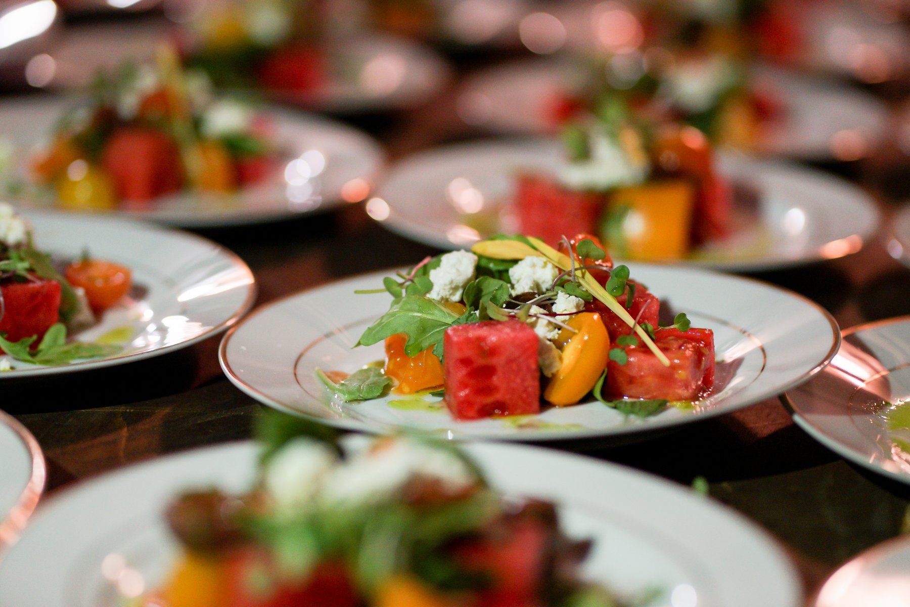 Rows of plated heirloom tomato and watermelon salads at a Hamptons benefit dinner produced by Golden Circle's principal