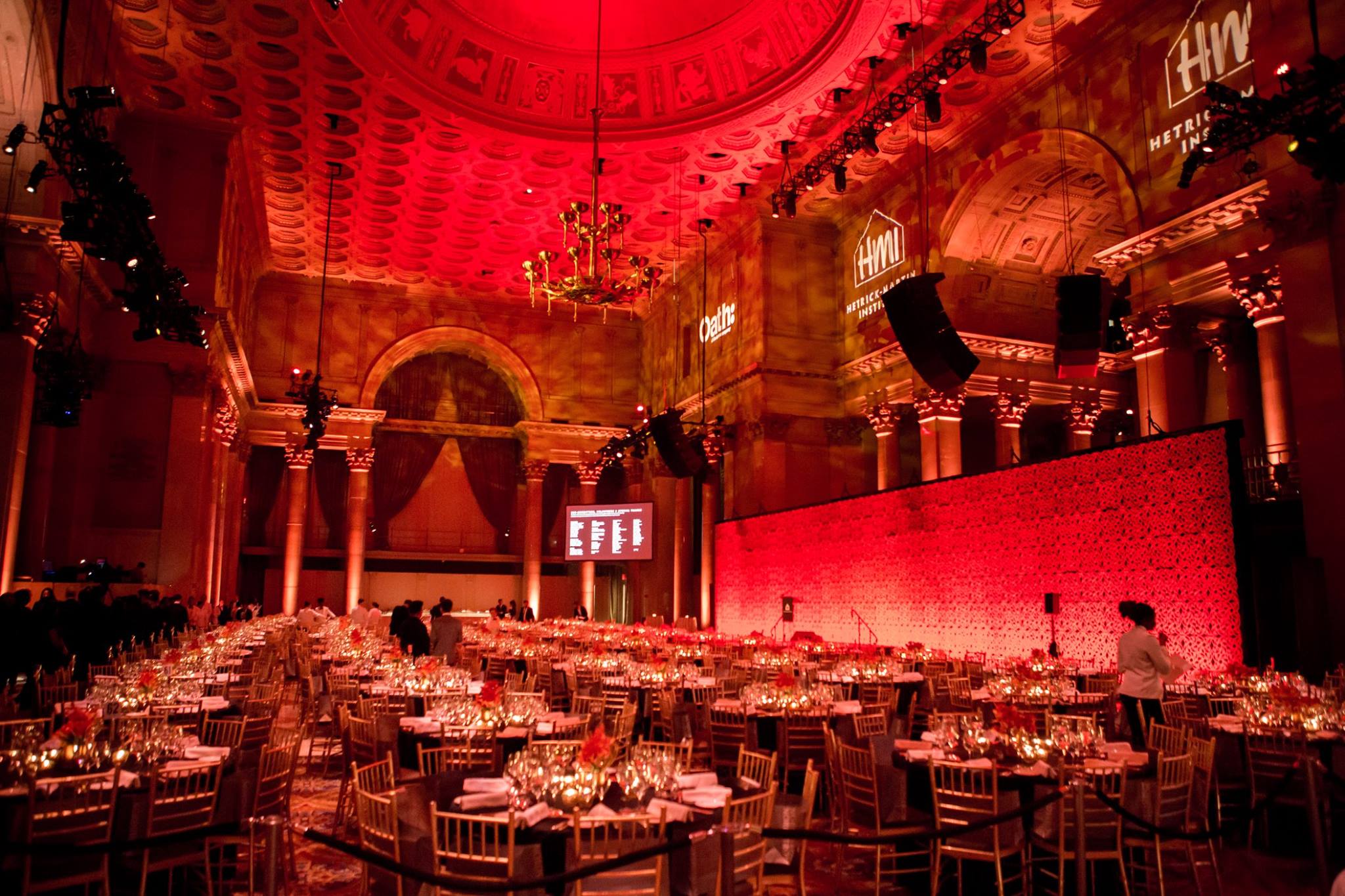 A grand landmark ballroom bathed in red light, set for a New York City gala produced by Golden Circle's principal, with gilded columns and a domed ceiling